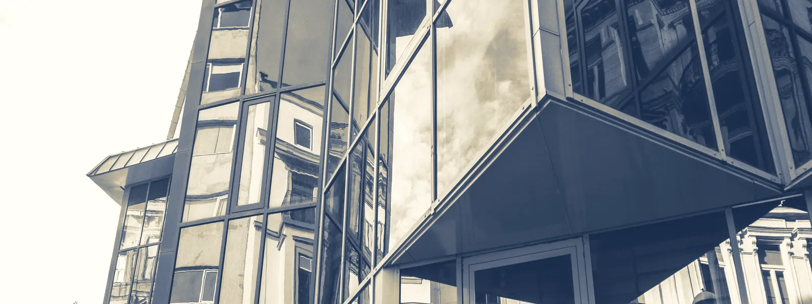 Fachada de vidrio de un edificio moderno que refleja construcciones antiguas, en duotono azul